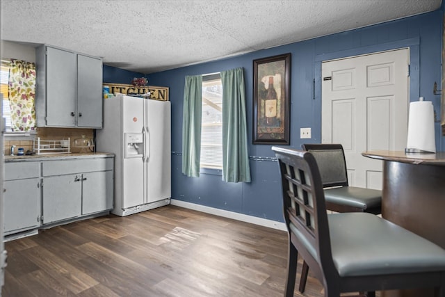 kitchen featuring baseboards, white refrigerator with ice dispenser, light countertops, a textured ceiling, and dark wood-type flooring