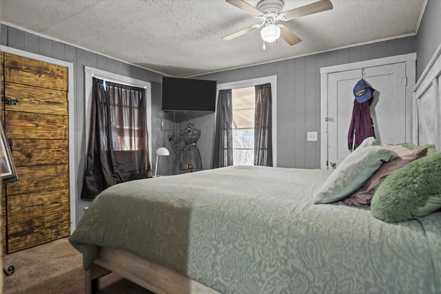 carpeted bedroom with wooden walls, a ceiling fan, and a textured ceiling