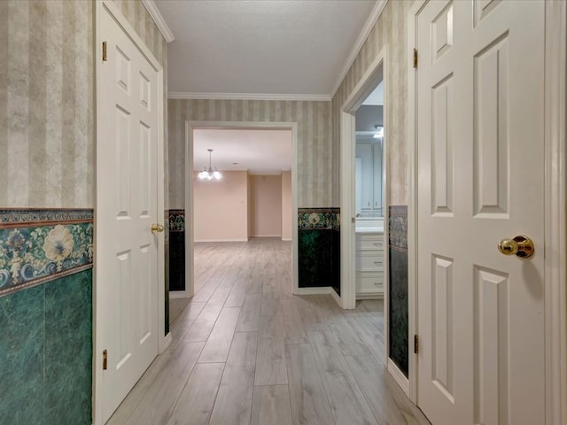 hallway with ornamental molding, light hardwood / wood-style floors, a textured ceiling, and an inviting chandelier