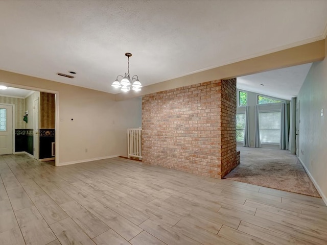 spare room featuring lofted ceiling, light wood-type flooring, brick wall, and a chandelier