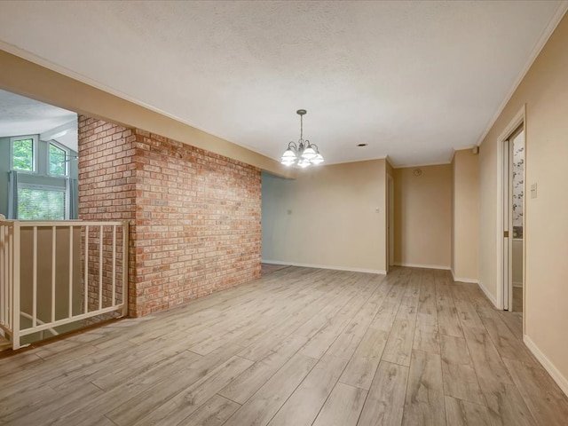 unfurnished room with an inviting chandelier, light hardwood / wood-style floors, brick wall, and ornamental molding