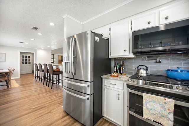 1405 Oak Hill Pl, Lufkin, TX 75904 - kitchen featuring appliances with stainless steel finishes, decorative backsplash, white cabinets, light wood finished floors, and a textured ceiling