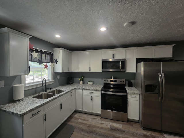 kitchen with white cabinets, sink, a textured ceiling, appliances with stainless steel finishes, and wood-type flooring