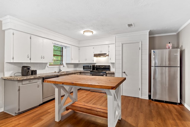 kitchen with sink, stainless steel appliances, wood-type flooring, decorative backsplash, and white cabinets