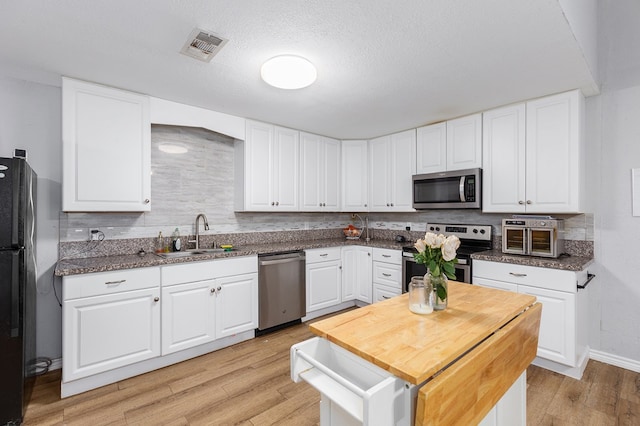 240 W 7th St, Trinity, TX 75862 - kitchen featuring appliances with stainless steel finishes, a sink, light wood-type flooring, tasteful backsplash, and a textured ceiling