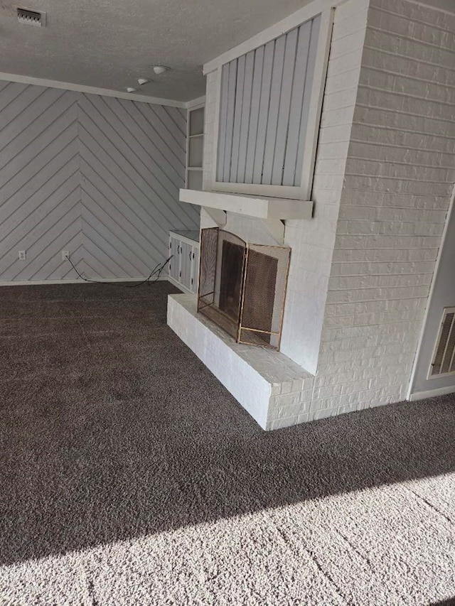 unfurnished living room featuring visible vents, a fireplace with raised hearth, a textured ceiling, carpet, and wood walls