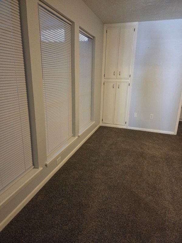 unfurnished bedroom with dark carpet and baseboards