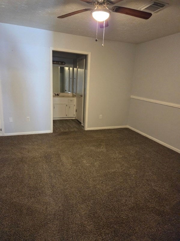 empty room featuring visible vents, a textured ceiling, dark colored carpet, baseboards, and ceiling fan