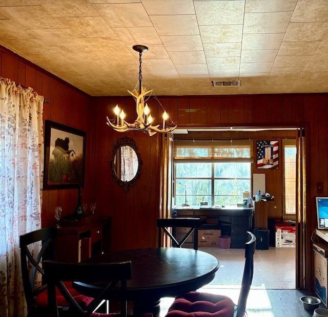 dining space with a chandelier and wood walls