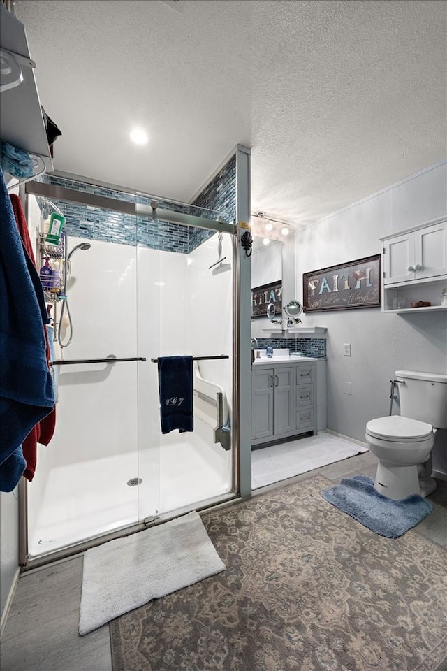 bathroom with vanity, toilet, a shower with door, and a textured ceiling