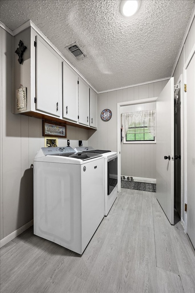 laundry room with washer and dryer, cabinets, a textured ceiling, and light hardwood / wood-style flooring