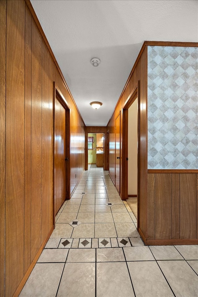 hallway with wooden walls, light tile patterned flooring, and ornamental molding