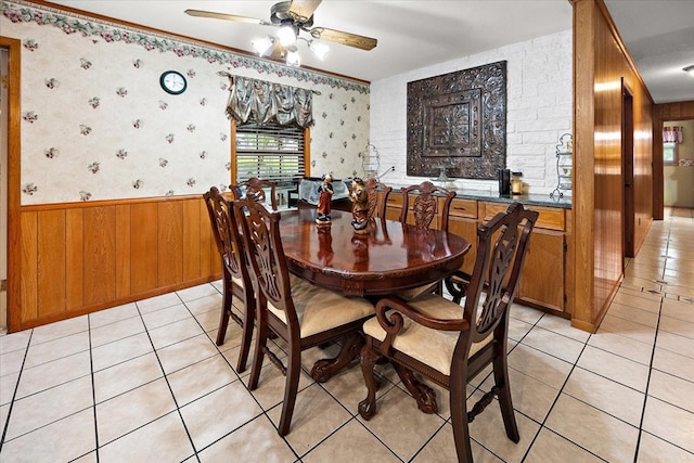 dining space with wood walls, ceiling fan, light tile patterned floors, and ornamental molding