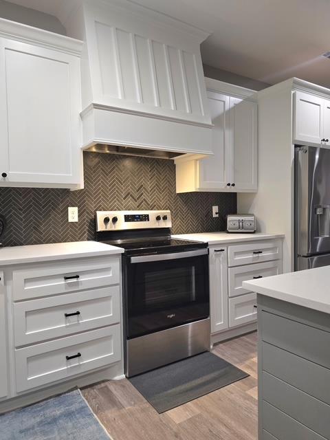 kitchen featuring appliances with stainless steel finishes, light countertops, light wood-style flooring, white cabinetry, and custom range hood