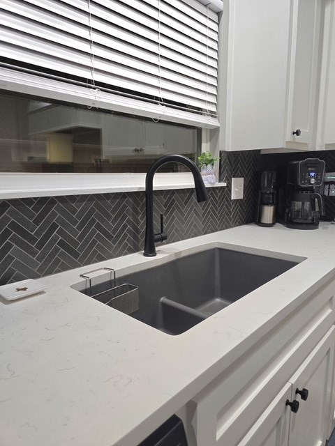 kitchen featuring a sink, backsplash, white cabinets, and light stone countertops