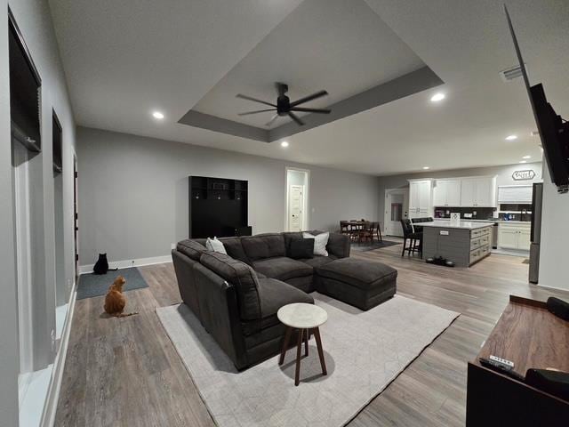 living area featuring light wood-style floors, recessed lighting, a raised ceiling, and ceiling fan