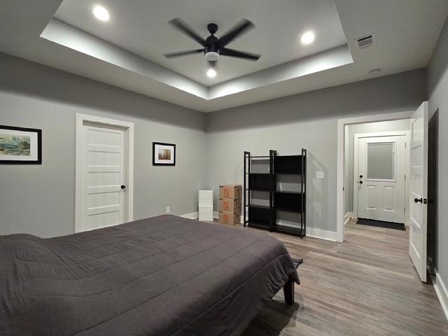 bedroom featuring a raised ceiling, light wood-style floors, recessed lighting, baseboards, and visible vents