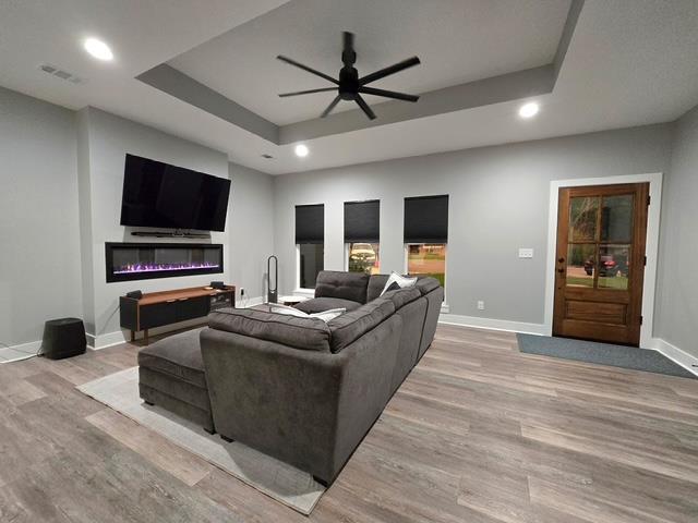 living room with ceiling fan, visible vents, light wood-type flooring, baseboards, and a tray ceiling