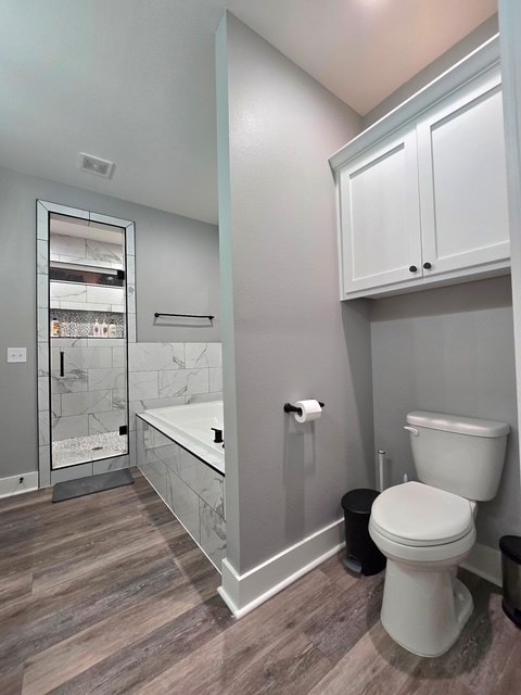 bathroom featuring wood finished floors, toilet, baseboards, a bath, and a shower stall