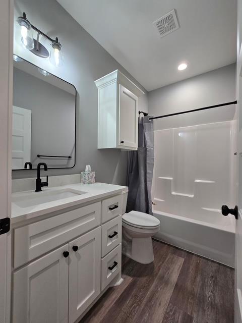 bathroom featuring visible vents, wood finished floors, vanity, toilet, and shower / bath combo with shower curtain