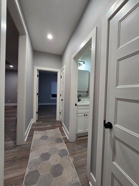 corridor with baseboards, a sink, dark wood-style flooring, and recessed lighting