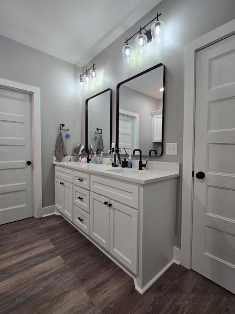 full bath featuring double vanity, a sink, baseboards, and wood finished floors
