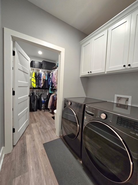 washroom featuring separate washer and dryer, cabinet space, and light wood-type flooring