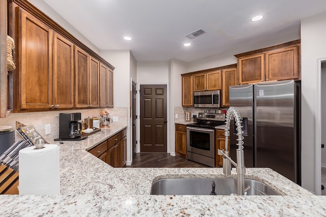 kitchen featuring sink, dark hardwood / wood-style floors, stainless steel appliances, light stone countertops, and backsplash