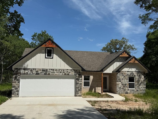 craftsman house with a shingled roof, board and batten siding, driveway, stone siding, and a garage
