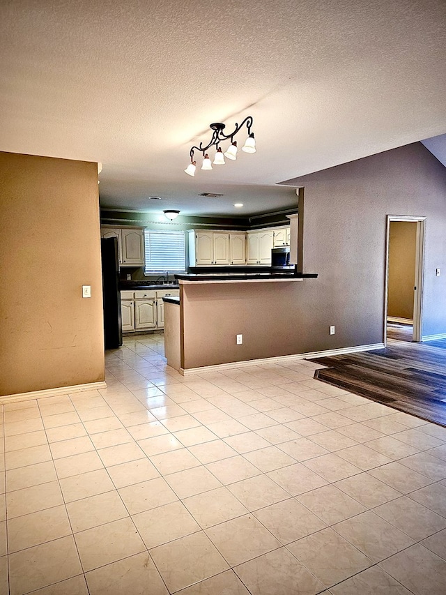 kitchen with cream cabinetry, black fridge, kitchen peninsula, and a textured ceiling