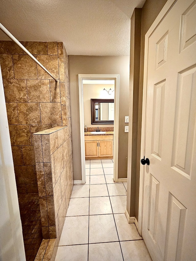 bathroom featuring tile patterned floors, vanity, tiled shower, and a textured ceiling