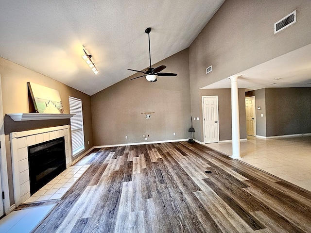 unfurnished living room with high vaulted ceiling, ceiling fan, a textured ceiling, a fireplace, and light hardwood / wood-style floors