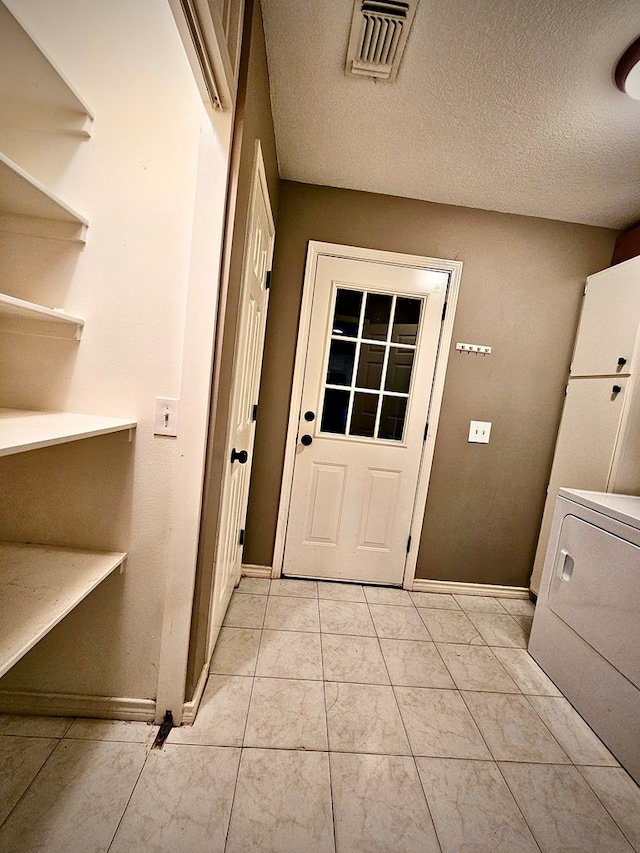 doorway with a textured ceiling, washer / clothes dryer, and light tile patterned flooring