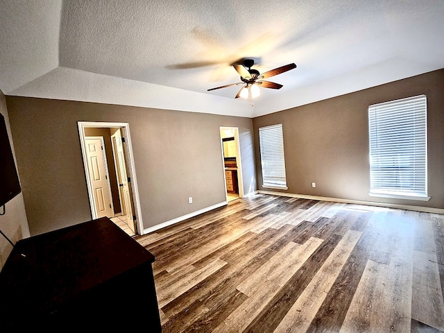 unfurnished bedroom with a textured ceiling, ceiling fan, wood-type flooring, and ensuite bathroom