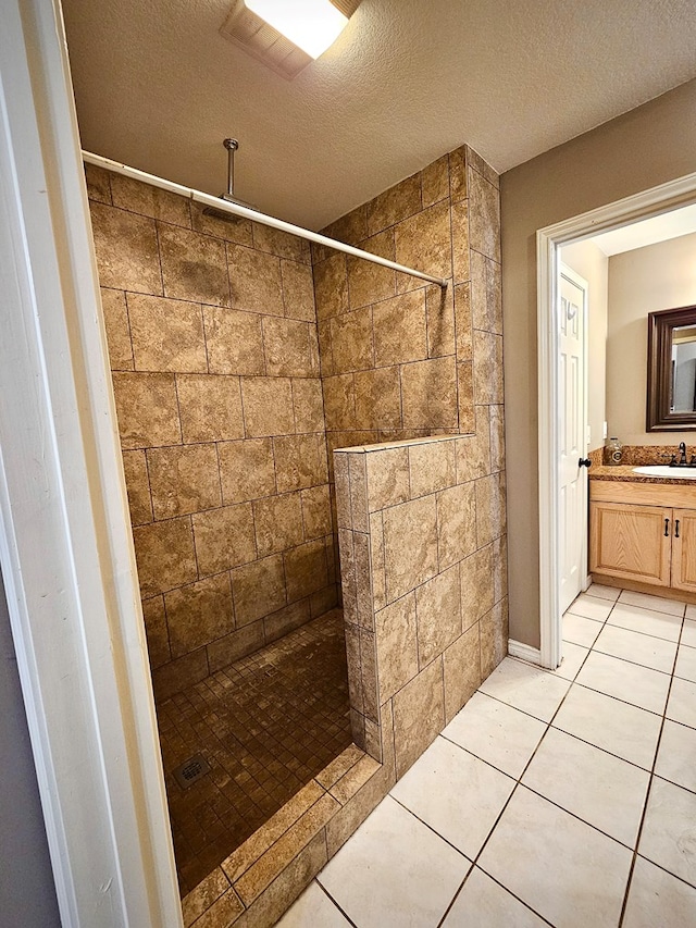 bathroom with a tile shower, tile patterned flooring, a textured ceiling, and sink