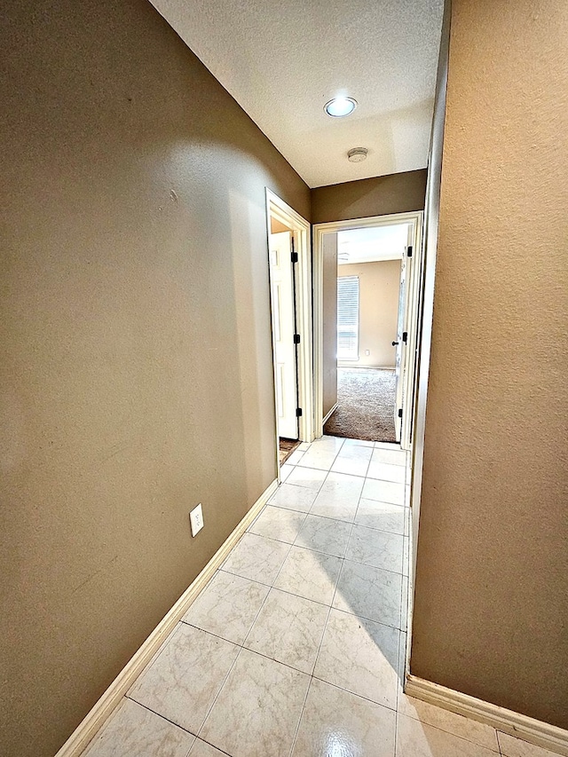 corridor with light tile patterned flooring and a textured ceiling