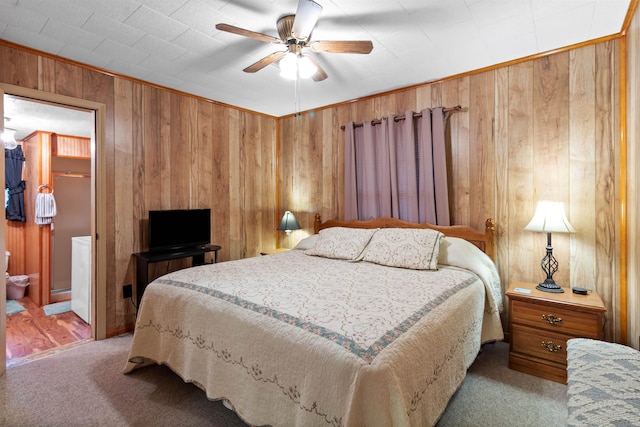 bedroom featuring carpet flooring, ensuite bath, ceiling fan, and wood walls