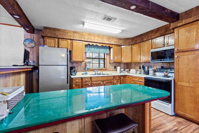 kitchen featuring sink, wooden walls, light hardwood / wood-style flooring, beam ceiling, and stainless steel appliances