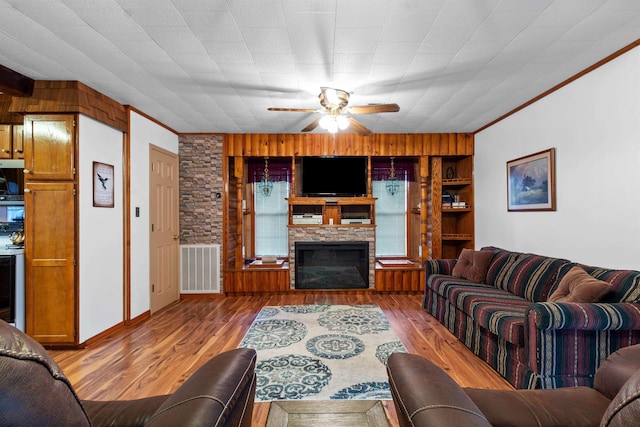 living room featuring a stone fireplace, ceiling fan, ornamental molding, and hardwood / wood-style flooring