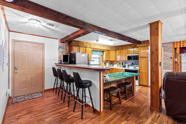 kitchen with stainless steel appliances, dark hardwood / wood-style flooring, beamed ceiling, kitchen peninsula, and a breakfast bar