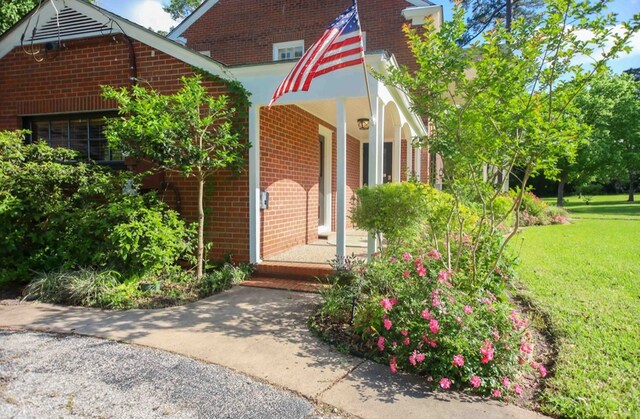 property entrance featuring a porch, a lawn, and brick siding