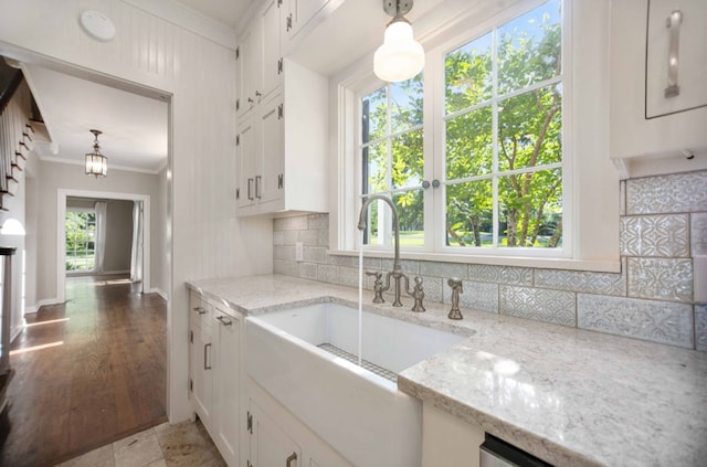 kitchen with light stone counters, white cabinetry, decorative backsplash, crown molding, and a sink