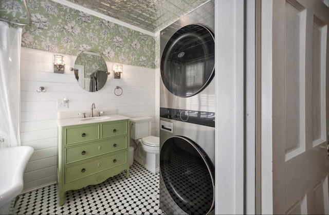 laundry area with a sink, stacked washer and clothes dryer, laundry area, an ornate ceiling, and wallpapered walls