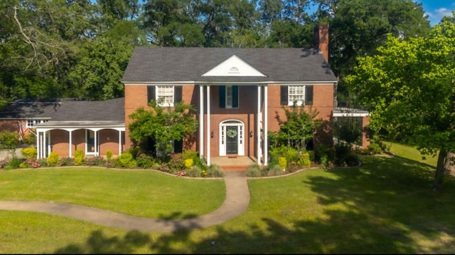 greek revival house featuring a chimney, brick siding, and a front lawn