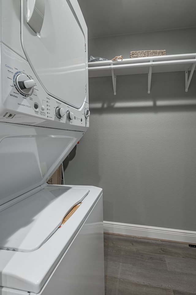 clothes washing area with baseboards, wood finished floors, stacked washer and dryer, and laundry area