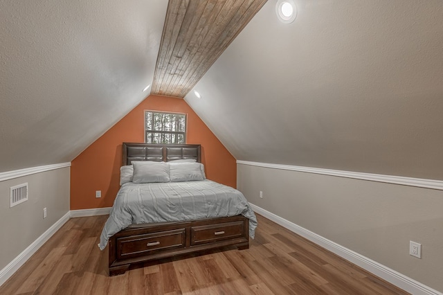 bedroom with lofted ceiling, visible vents, wood finished floors, and baseboards