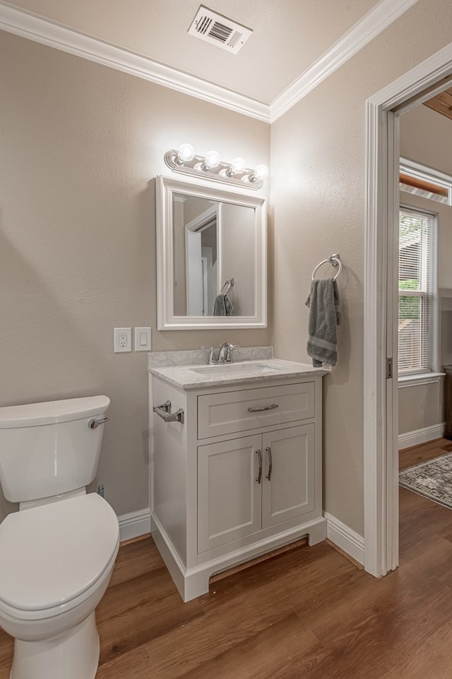 bathroom with crown molding, toilet, visible vents, baseboards, and wood finished floors