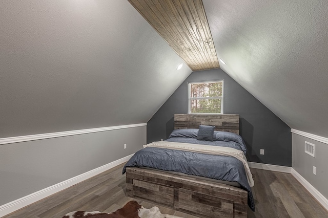 bedroom with lofted ceiling, a textured ceiling, wood finished floors, and visible vents
