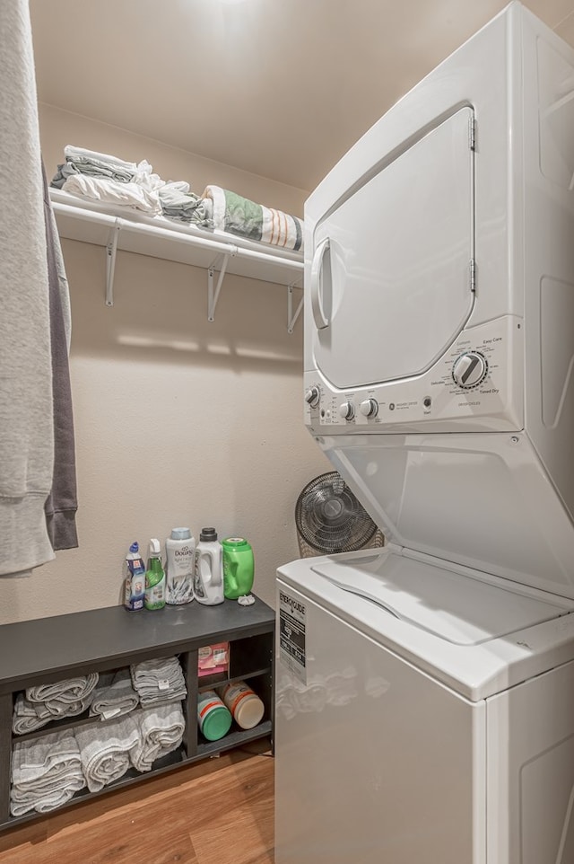 clothes washing area with stacked washing maching and dryer, wood finished floors, and laundry area