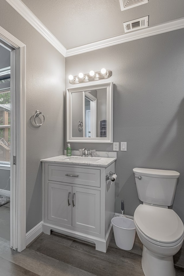bathroom with wood finished floors, toilet, vanity, baseboards, and crown molding
